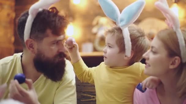 Szczęśliwa rodzina matki, ojca i syna malowała wielkanocne jajka, nosząc królicze uszy w Wielkanoc. śmieszne słodkie dzieci twarz. — Wideo stockowe