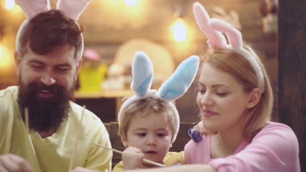 Великоднє сімейство матері, батька і сина розмальовували яйця, вдягаючи кролячі вуха. Сім'я святкує Великдень з дітьми вдома, батьки веселих великодніх кроликів. Смішні милі діти стикаються . — стокове відео