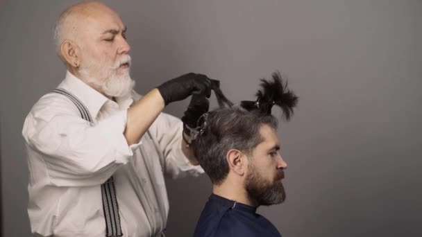 Processus d'un gars ayant les cheveux teints au salon de coiffure. Hipster barbu hommes teindre sa couleur de cheveux sur un fond gris. Coiffeur sénior sèche cheveux. — Video