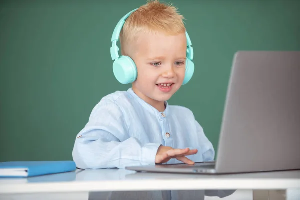 Menino pequeno em fones de ouvido assistir vídeo lição no computador na escola, criança em fones de ouvido têm aula on-line, usando laptop. Estudo remoto e educação. — Fotografia de Stock