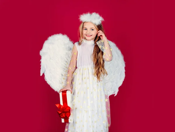 Kinderengel mit Geschenk, Studioporträt. Kleiner Engel mit weißen Flügeln hält Geschenk. Verspieltes engelhaftes kleines Mädchen. Valentinstag. — Stockfoto