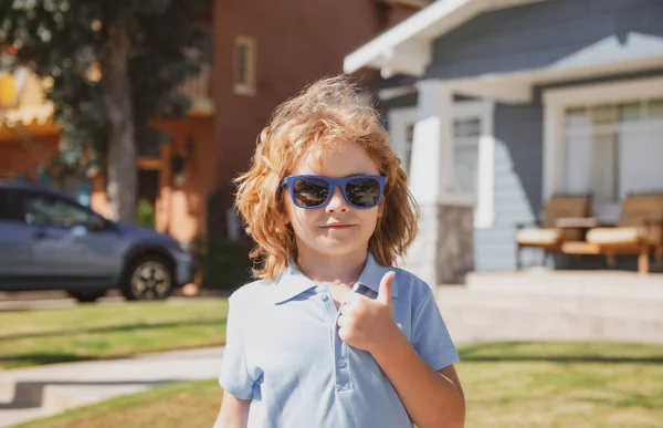 親指をサインアップしてサングラスで面白い子を閉じます。家の近くの子供の屋外の家頭部の肖像画. — ストック写真