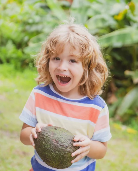 Criança comendo e desfrutando de um abacate em um fundo de natureza. Alimentos saudáveis para crianças conceito. — Fotografia de Stock