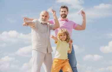 Çocuklarla aktif aile eğlencesi. Oğlu babası ve büyükbabası ile oyuncak uçağıyla yaz gökyüzü arka planında oynuyor. Aile macerası, hayal gücü, yenilik ve ilham.
