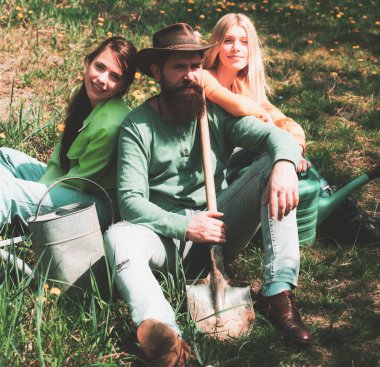 Bahar bahçesinde çimlerde oturan arkadaşlar. Kafkas erkek çiftçi portresi, elinde kürekle iki arkadaş kızla. Sıkı çalışmadan sonra dinleniyor..