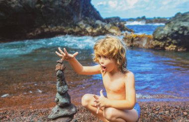 Heyecanlı çocuk çakıl taşı plajında taş piramit yapıyor. İstikrarı, zen 'i, ahengi ve dengeyi simgeliyor..