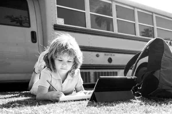 Schlauer Schüler auf dem Rasen mit digitalem Tablet im Schulpark. Kind benutzt Geräte, um im Freien zu lernen. Bildung und Lernen für Kinder. — Stockfoto