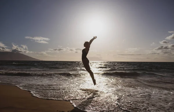 一个无忧无虑的女人，高举双手，在大海和蓝天的映衬下跳跃着。暑假、旅行和自由的概念. — 图库照片