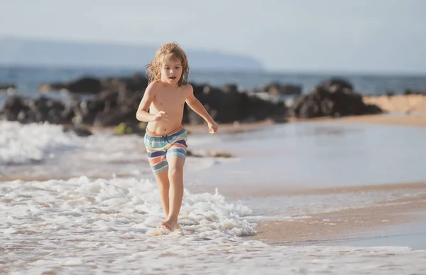 Ragazzo corridore divertirsi sulla spiaggia tropicale del mare. Bambino divertente correre con spruzzi di acqua piscina lungo il bordo surf. Attività per bambini durante le vacanze estive. — Foto Stock