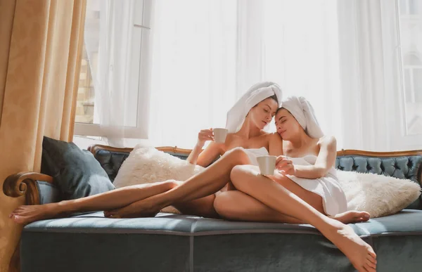 Αισθησιακές λεσβίες φιλενάδες. Νεαρές όμορφες σέξι γυναίκες με λευκά μπουρνούζια και πετσέτες στην κρεβατοκάμαρα. Carefree γυναικεία μοντέλα στο κρεβάτι στο διαμέρισμα ή το δωμάτιο του ξενοδοχείου. Πρωινή ψύχρα. — Φωτογραφία Αρχείου