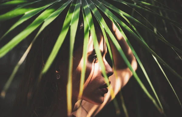 Sexig vacker kvinna som gömmer sig bakom palmbladen. Vacker hona som rör ansiktet med ömhet. Ung kvinna poserar. Perfekt hud. Ansiktsbehandling. Skönhet och mode koncept. Hudvård. — Stockfoto