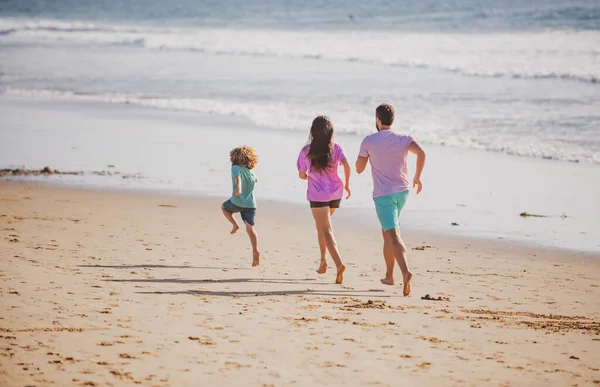 幸せな家族の父、母と赤ちゃんの息子が一緒に楽しみを持って、黒砂のビーチで海の波に沿って水プールで実行されます。夏休みに子供と一緒に旅行ライフスタイル、両親. — ストック写真