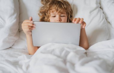Çocuklar internet. Yatakta tabletli çocuk. Ebeveyn izni, güvenlik ağı. Çocuk oyun oynuyor. Sosyal ve teknoloji kavramı.