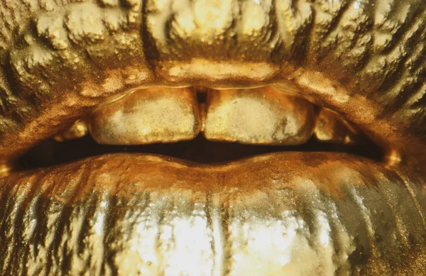 Macro close up gold lips. Gold paint from the mouth. Golden lips on woman mouth with make-up. Sensual and creative design for golden metallic.