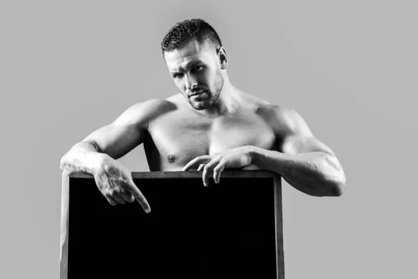 Hombre de fitness con cartel publicitario. Guapo musculoso culturista sosteniendo cartel en blanco aislado sobre fondo gris. —  Fotos de Stock