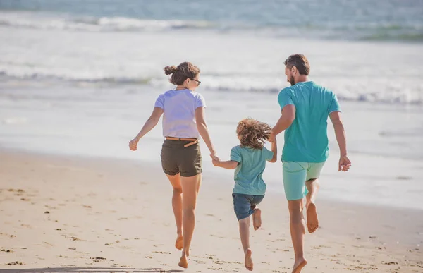 快乐的年轻家庭在夏天的海滩上奔跑和跳跃。父母跑着跳着的孩子。健康假日和家庭活动. — 图库照片
