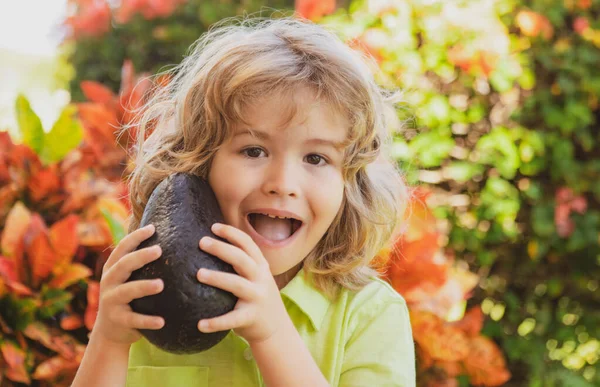 Criança feliz mostrando abacate no jardim de verão. Crianças comida saudável. — Fotografia de Stock