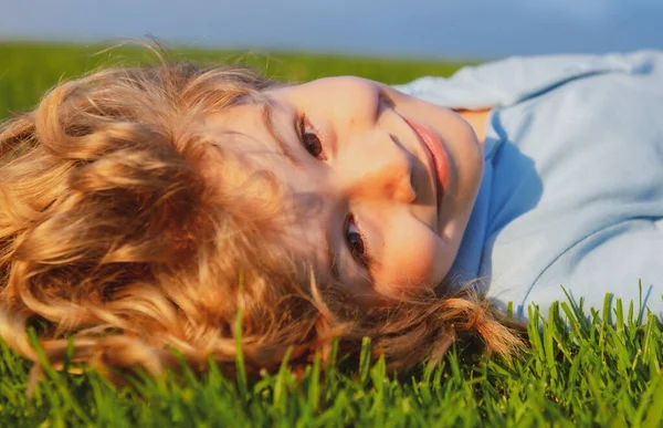 Porträtt av en leende liten pojke liggande på grönt gräs. Leende pojke som har roligt utomhus i vårträdgården. — Stockfoto