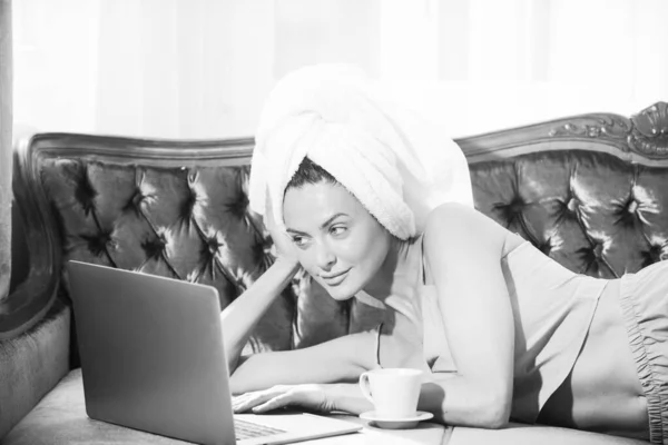 Attraente studentessa in pigiama e asciugamani che studiano a casa, usando il computer portatile, bevendo caffè. — Foto Stock