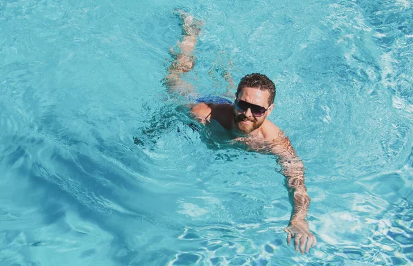 Hombre en vacaciones de verano. Un tipo con gafas de sol nadando en la piscina. Summertime piscina resort. — Foto de Stock