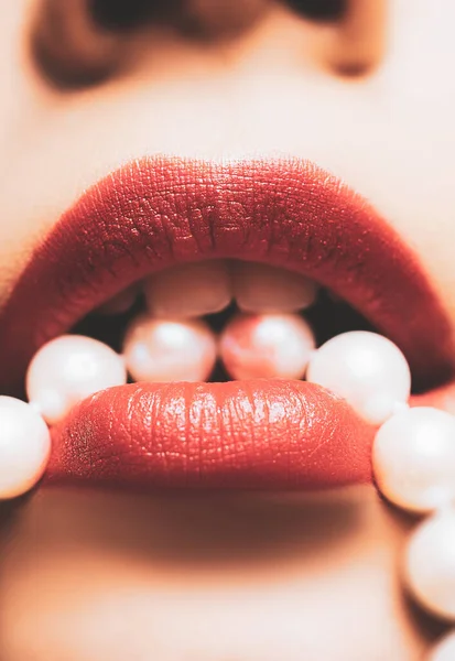 Sexy heldere rode vrouw lippen houden parel ketting close-up foto. Vrouwelijke lippen met luxe oranje rode lippenstift. Vrouw met parelsnoer in de mond close-up foto. — Stockfoto