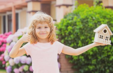 Mutlu çocuk yeni evine karşı oyuncak evi elinde tutuyor. Çocuklar için konut kavramı.