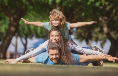 Hoş bir aile portresi. Parkta rahatlayan mutlu bir ailenin portresi. Aile parkta çimlerin üzerinde yatıyor. Uç kavramı, küçük çocuk uçuşu taklit ederken kazma gibi oturuyor..
