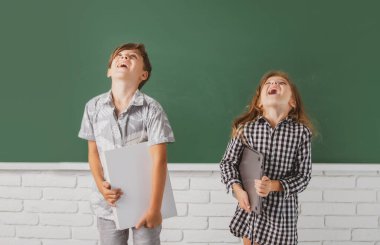 Okul çocukları kitabı karatahtaya karşı şaşırtıcı bir ifadeyle tutarlar. Okul çocukları arkadaşlar.