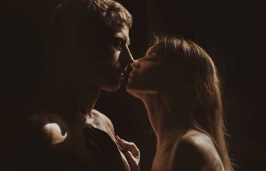 Birbirine aşık romantik bir çift birbirine bakar, sarılır ve siyah arka planda öpüşür..