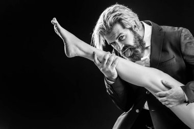 Takım elbiseli, kadın bacaklı bir erkek. Ayak fetişi olan adam bacağını yalıyor. Lüks ve ataerkil.