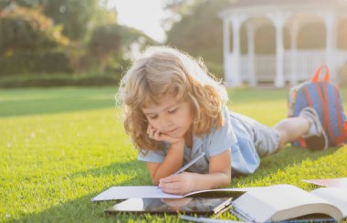 Çimen arka planı üzerine kitap yazan güzel bir çocuk. Çocuklar parkta kitap okuyor..