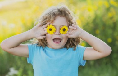 Yazın doğa parkında gözlerinin önünde çiçek tutan heyecanlı çocuğun portresi. Çocuk kavramı yakın planda. Çocuklar yazın tadını çıkarıyor. Gözleri çiçek konseptiyle kaplar.