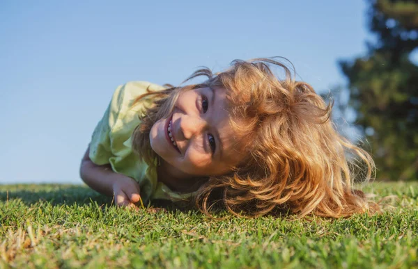 Happy little blond child laying on the grass in the park. Smmer day during school holidays. Amazed kid boy dreaming and smiling outdoor. — Stock Photo, Image