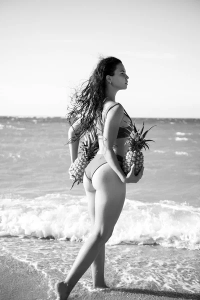 Szexi nő friss ananásszal a kezében. Buttocks lány bikini gyümölcs ananász a tengerparton háttér, nyári vakáció, egészséges ételek és fitness. — Stock Fotó