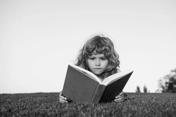 Criança com um livro no jardim. Sucesso de crianças, conceito de líder de sucesso. Kid está lendo um livro tocando ao ar livre no dia de verão. — Fotografia de Stock