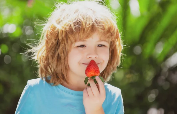 Jídlo pro zdravé děti. Roztomilý chlapec jí jahodu na zeleném letním pozadí. Zavřít děti šťastný obličej. — Stock fotografie