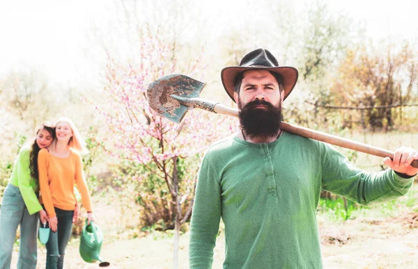 Hombre barbudo plantando plantas en el jardín de primavera. Trabajo en equipo y amigos concepto de unidad . —  Fotos de Stock