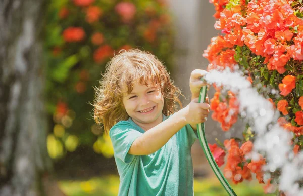 Το παιδί που παίζει στον κήπο, χύνει από το λάστιχο και βρέχει. Χαρούμενη παιδική ιδέα. Το παιδί ρίχνει νερό στα δέντρα. Παιδική φροντίδα για τα φυτά στην πίσω αυλή. — Φωτογραφία Αρχείου