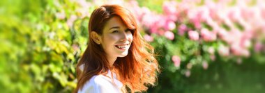 Pankart ya da web sitesi başlığı olarak güzel kadın yüzü olan bahar tasarımı, kopyalama alanı. Çiçek açan arka planda duran kızıl saçlı güzel bir kızın yakın portresi. Bahçedeki kadın.