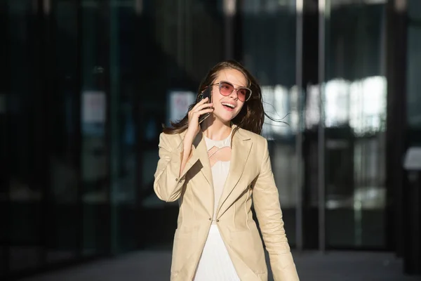 Счастливая взволнованная бизнес-леди в стиле разговора по телефону на открытом воздухе. Сексуальная девушка в повседневном платье ходит по улице. — стоковое фото