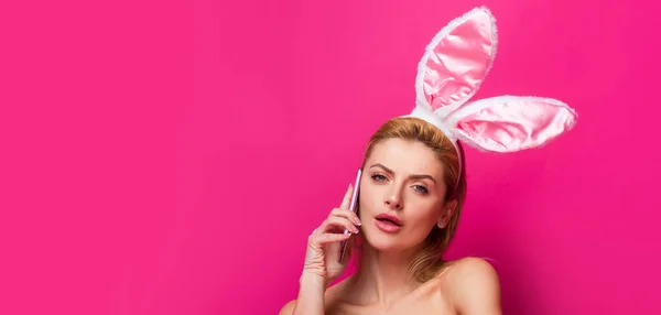 Sztandar wielkanocny z króliczką. Wielkanocna kobieta z króliczymi uszami rozmawiająca przez telefon, odizolowana na różowo. — Zdjęcie stockowe