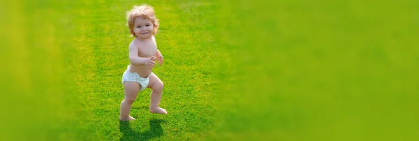 Banner med vårbarns ansikte. Första steget. Baby stående barfota på den gröna gräsmattan i blöja byxor. Barn på grönt gräs bakgrund. — Stockfoto