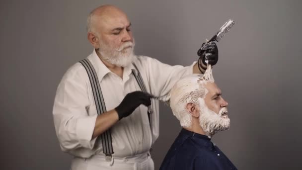 スタジオでプロの美容師乾燥髪。美容室で染め髪を持つ男のプロセス。ヒップスター髭の男は彼の髪の色を灰色の背景に染め. — ストック動画