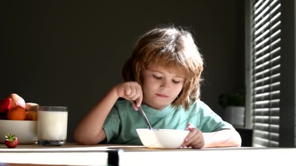 Dzieci jedzą owsiankę i mleko na śniadanie. Słodki chłopiec jedzący zdrowe jedzenie łyżką w domu. Jedzenie i picie dla dzieci. — Wideo stockowe