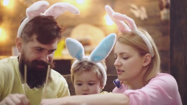 イースターエッグドローイングのコンセプト。母、父と子の息子のイースターの家族は、ウサギの耳を着て卵を描いた。家族自宅で子供たちとイースターを祝う,面白いイースターウサギの両親. — ストック動画
