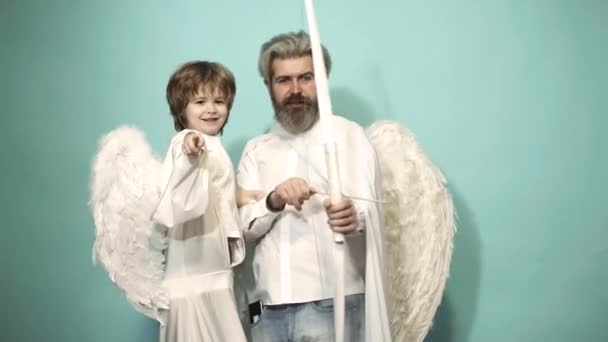 Valentin πατέρας και γιος άγγελοι με φτερά που στοχεύουν με τόξο και βέλος σε μπλε φόντο. Ευτυχισμένη οικογένεια και την ημέρα του Αγίου Βαλεντίνου έννοια. Γονέας, γονιός με παιδί αγόρι, παιδική ηλικία. — Αρχείο Βίντεο