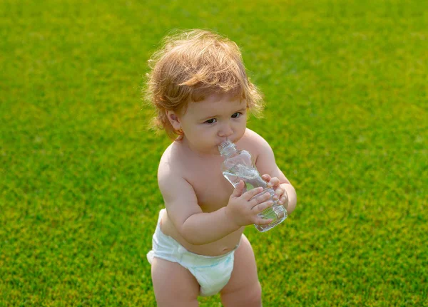 赤ん坊はボトルからミネラルウォーターを飲む。芝生の公園で休んでいる子供. — ストック写真