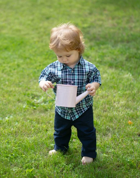 Lindo niño pequeño regando flores con regadera. Retrato de lindo niño caucásico divirtiéndose en el jardín. Niño en césped de hierba verde durante el paseo en el patio. Feliz infancia y cuidado del bebé —  Fotos de Stock