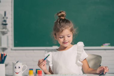 Okuldaki çocuk boyalarla resim çiziyor. Çocukların yaratıcılığı. Çocukluk eğitimi, çocukların sanatsal becerileri..