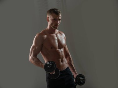 Sportif gövde, dambılı adam. Karanlık stüdyoda dambılla egzersiz yapan genç bir sporcunun portresi. Crossfit, spor ve sağlıklı yaşam tarzı konsepti.
